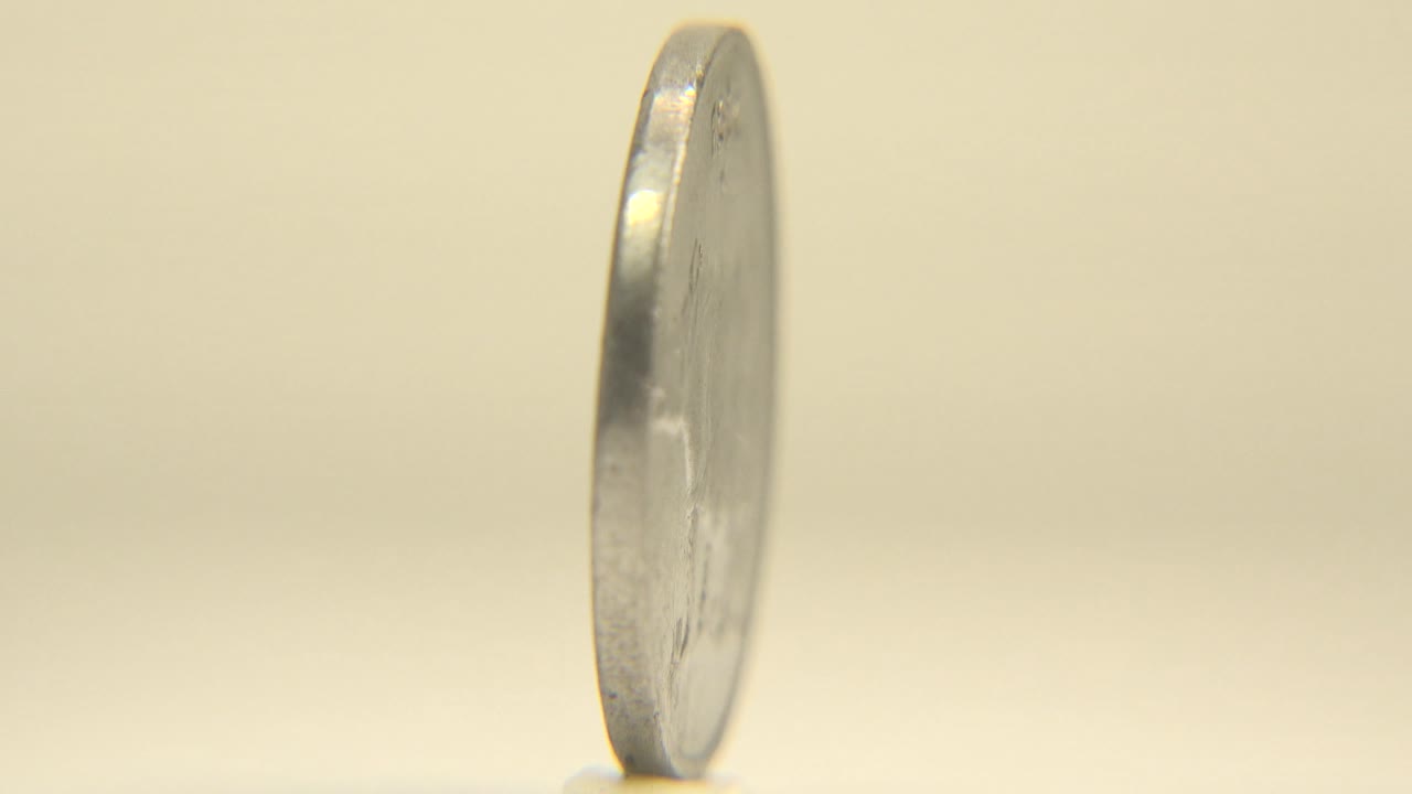 Silver coin seen mostly edge-on while standing upright.