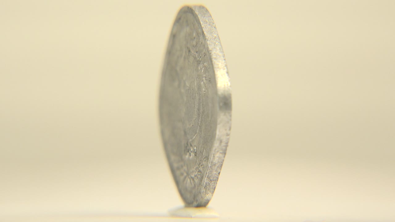 The coin remains upright on its edge, slightly rotated so faint Arabic markings are visible through the shallow focus, with no visible people.