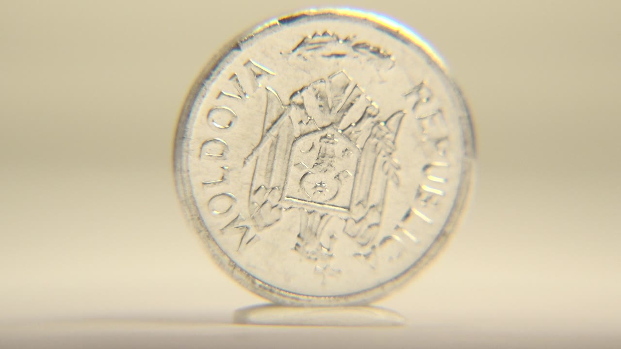 A silver five bani Moldovan coin stands upright on its edge with the coat of arms side facing camera, warm beige background, and no visible people.