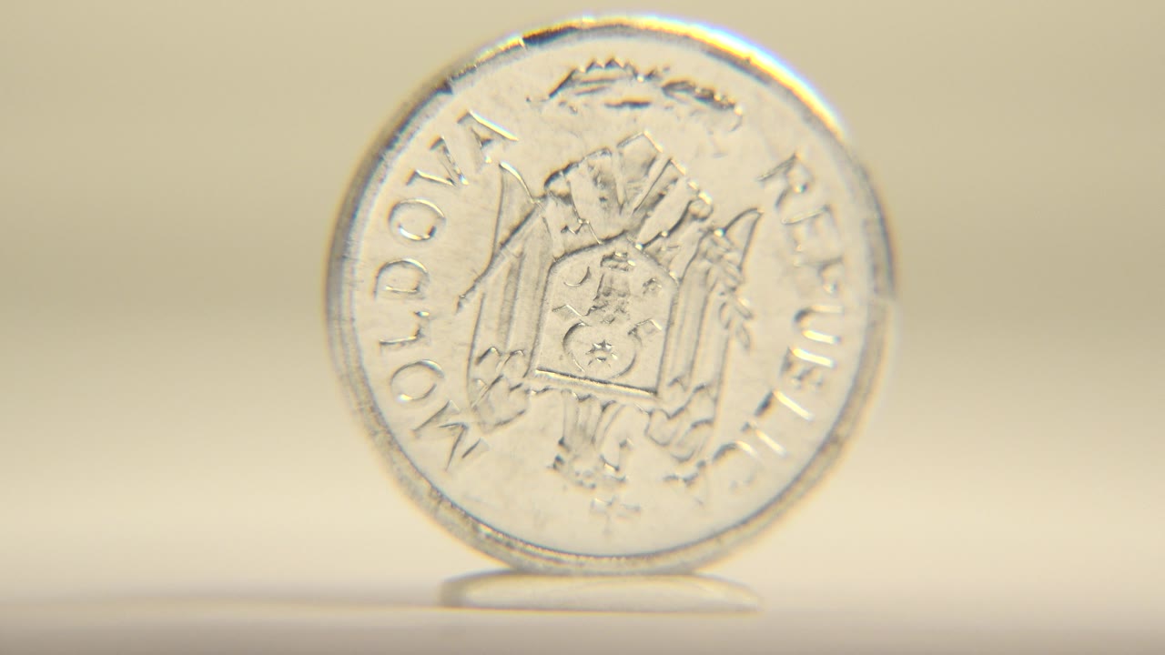 The upright silver coin remains near the center of the frame with the Moldovan coat of arms side still visible and slightly shifted angle, with no visible people.