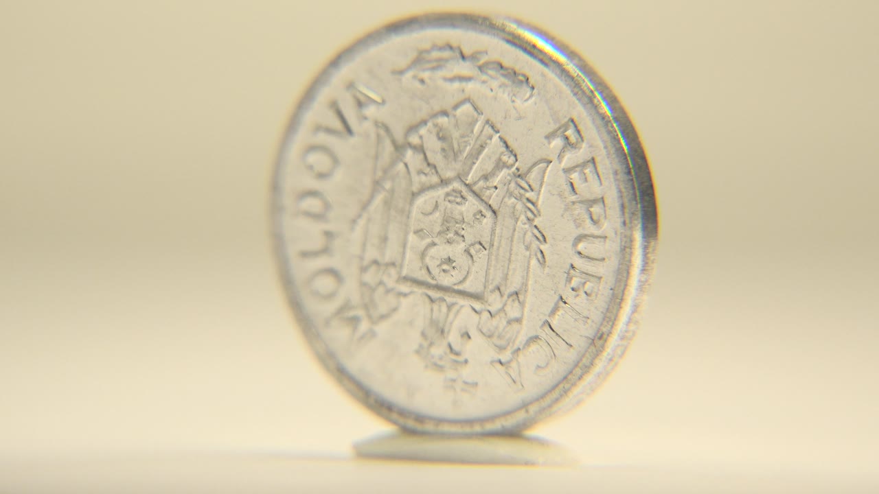 A five bani Moldovan coin appears slightly angled while standing on its edge, with the coat of arms side and rim text visible against a plain warm background and no visible people.