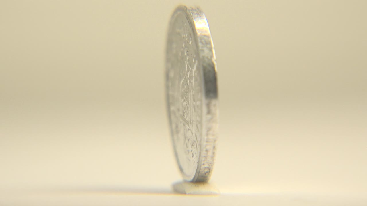 The coin turns nearly edge-on, reducing the face detail to a narrow silver profile above the pale surface, with no visible people in frame.
