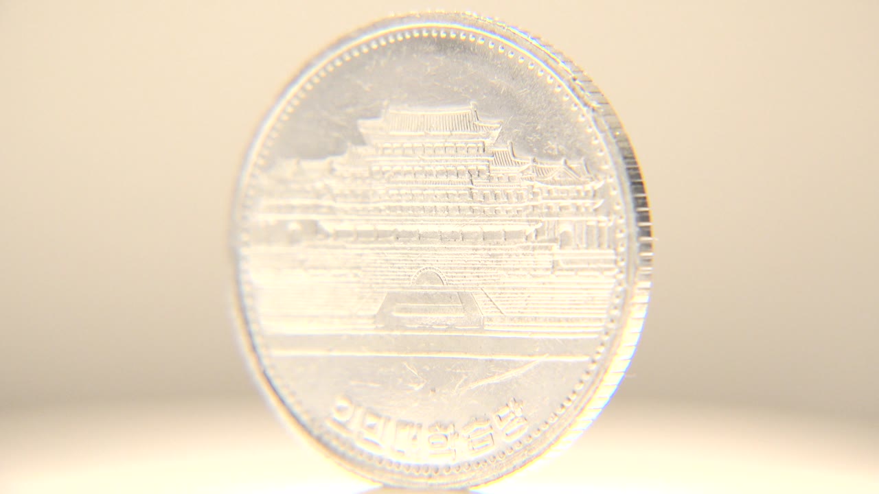 The same upright coin catches stronger light, washing out part of the building relief while its circular edge and Korean lettering remain visible, with no visible people.