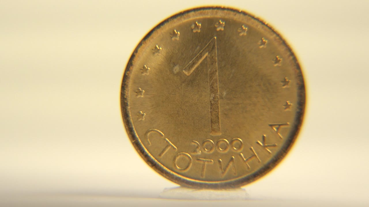 The coin remains nearly front-facing on the pale rotating surface, with warm highlights across the worn metal and no visible people.