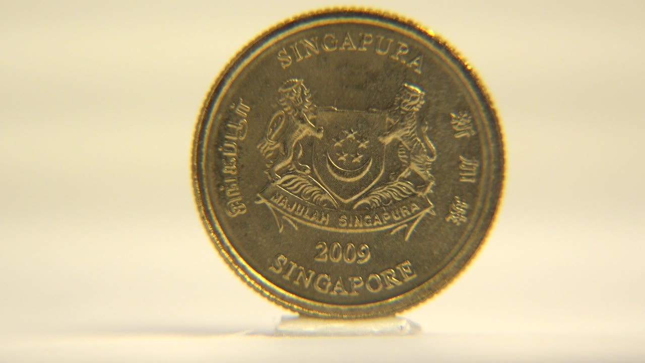 An upright five cent coin faces the camera on a white surface with Singapore text and crest details visible, no visible people.