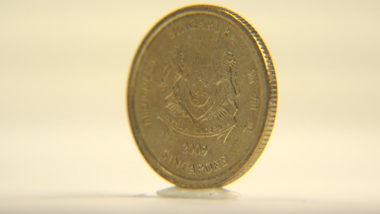 The upright coin has rotated to a slight angle, making the face darker and narrower while the ridged edge begins to show, no visible people.
