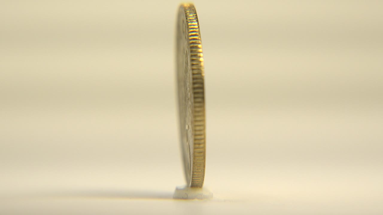 At 0:01, the upright Singapore coin remains in a slim side view, its ridged edge catching light against a soft cream background with no visible people.