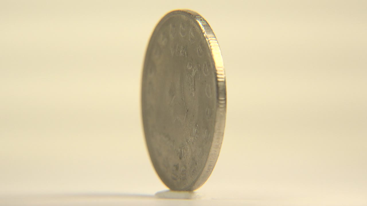 The coin is seen mostly from the side, showing its thin ridged edge, blurred face detail, and a small shadow beneath it, with no visible people.