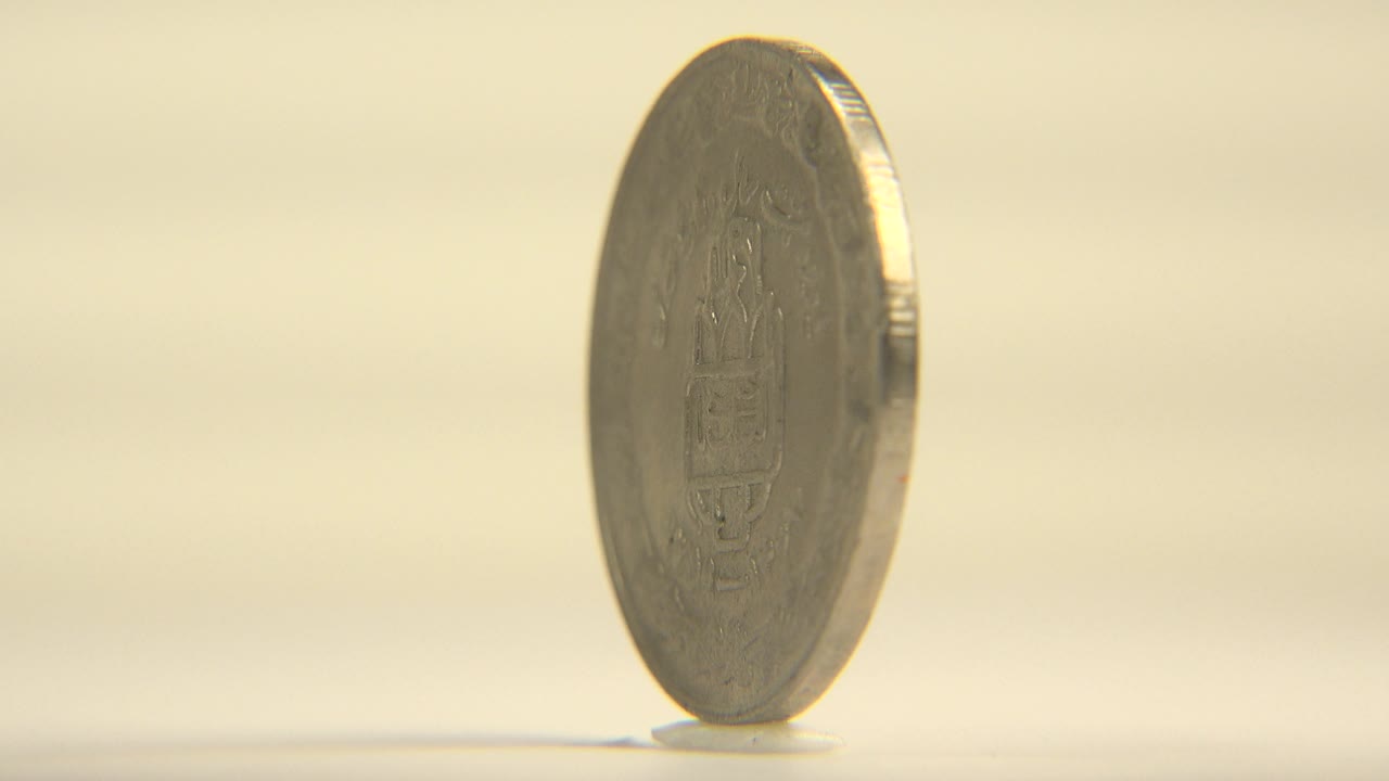 A silver coin stands upright on its edge near the center-left of a pale surface, with warm soft light and no visible people.
