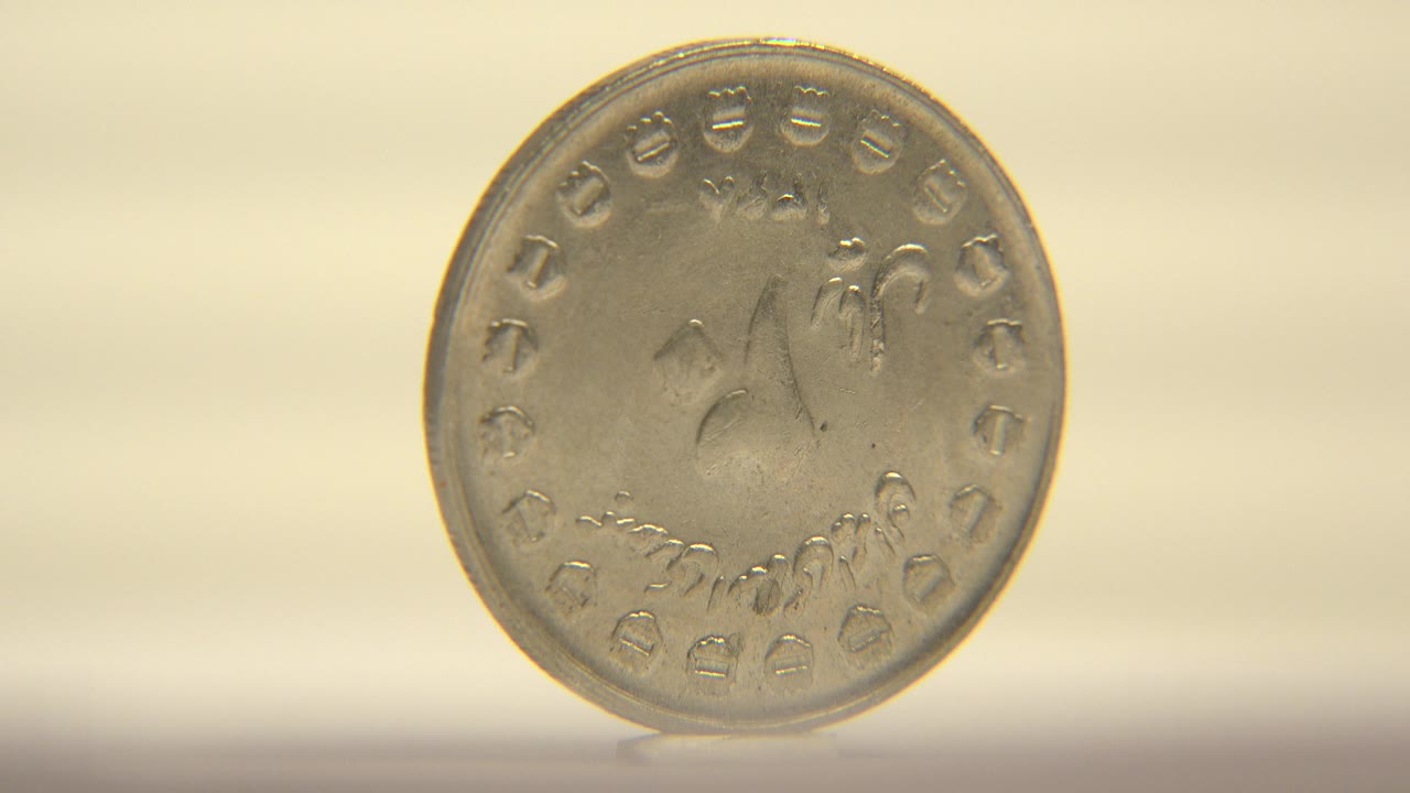 The coin turns toward camera, showing a flatter circular face with faint raised markings and warm reflections, with no visible people.