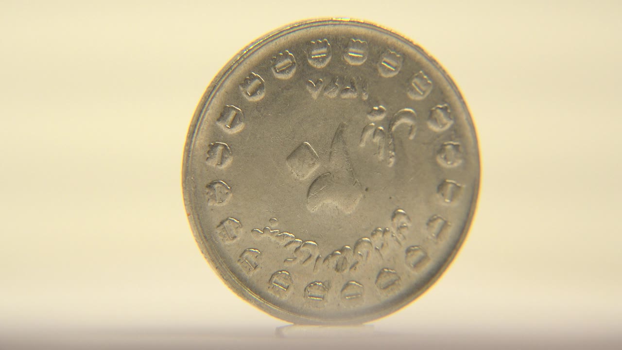 The coin remains upright and nearly front-facing, with raised markings around the rim and a warm cream background, with no visible people.