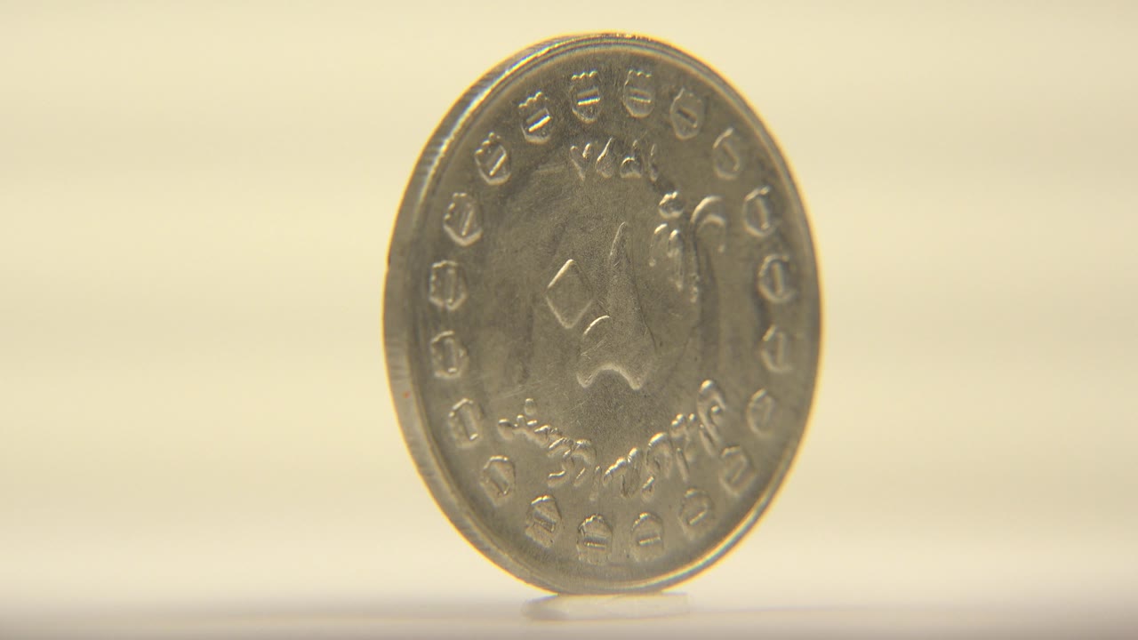 The coin remains upright and centered left of frame, showing a similar engraved face with subtle rotation and no visible people.