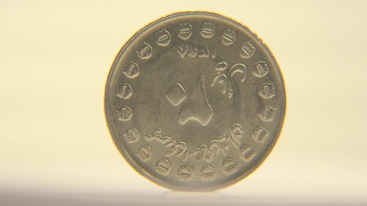 The rotating coin turns more toward the camera, making its round face appear wider against the soft cream background, with no visible people.