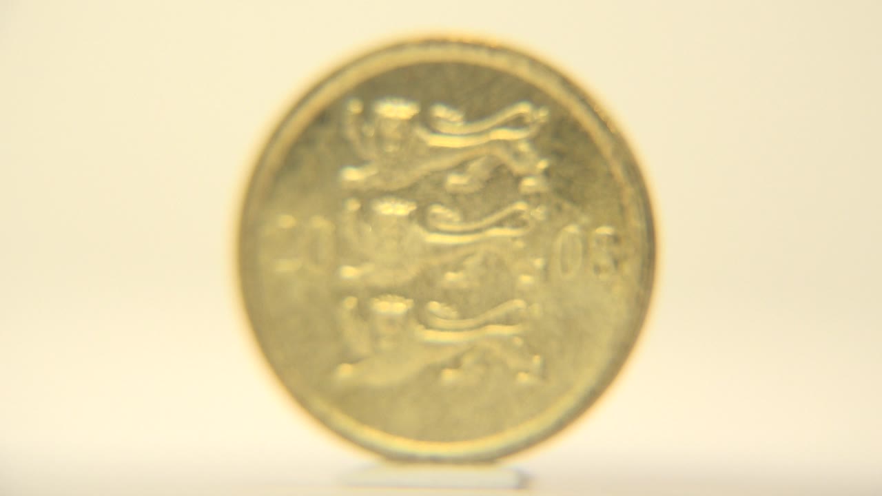 The Estonian coin is still presented almost face-on, with embossed symbols softened by shallow focus and no visible people.