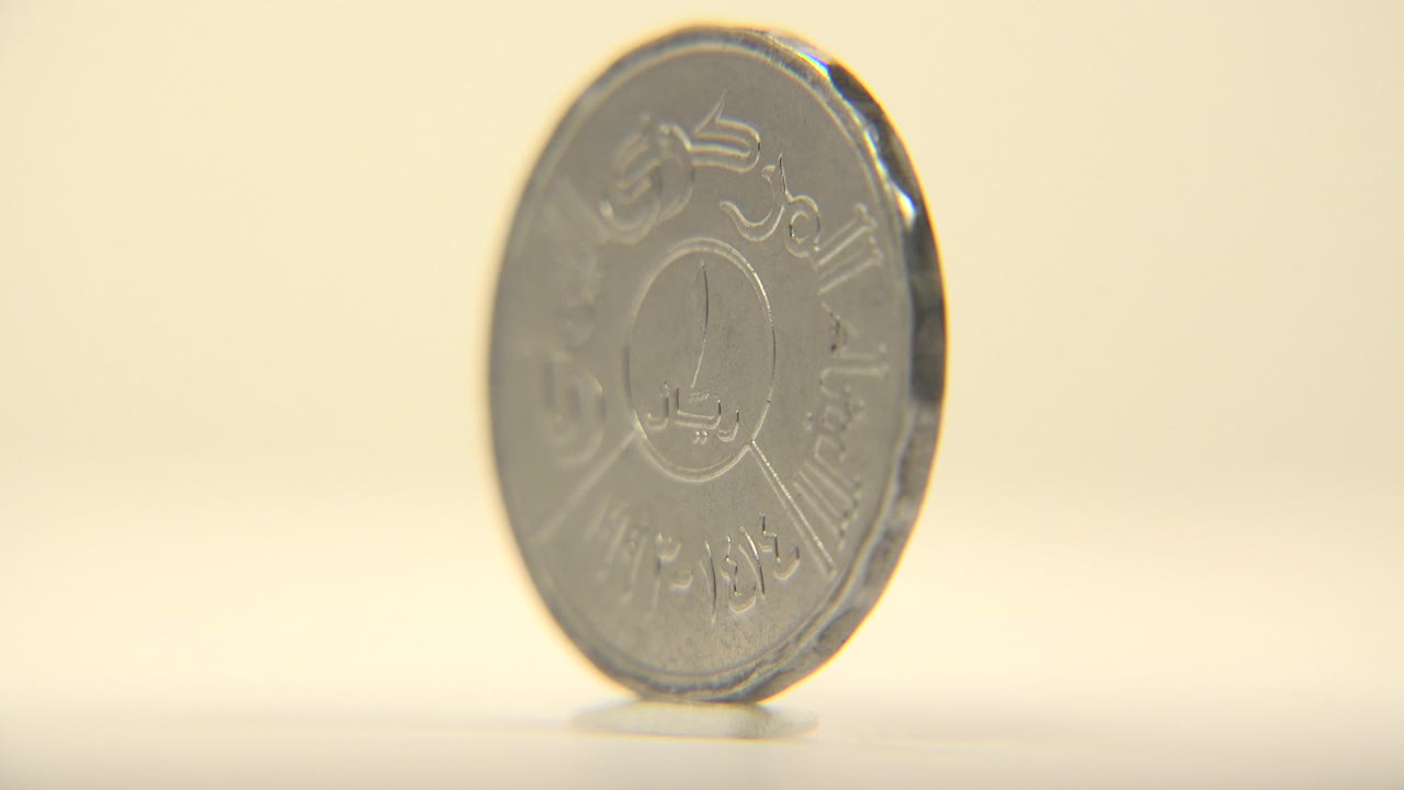 The coin remains upright and slightly angled, with the script side still visible and soft metal highlights along the rim, no visible people.
