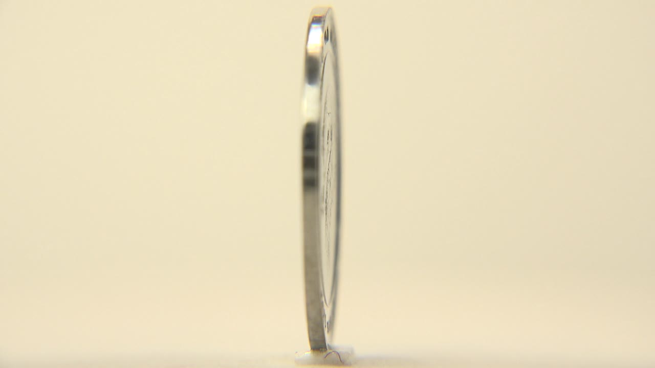 A narrow edge profile of the upright coin appears against the pale surface, emphasizing thickness and balance, no visible people.