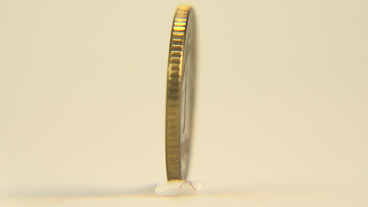 Narrow side view of a gold-colored coin standing upright.