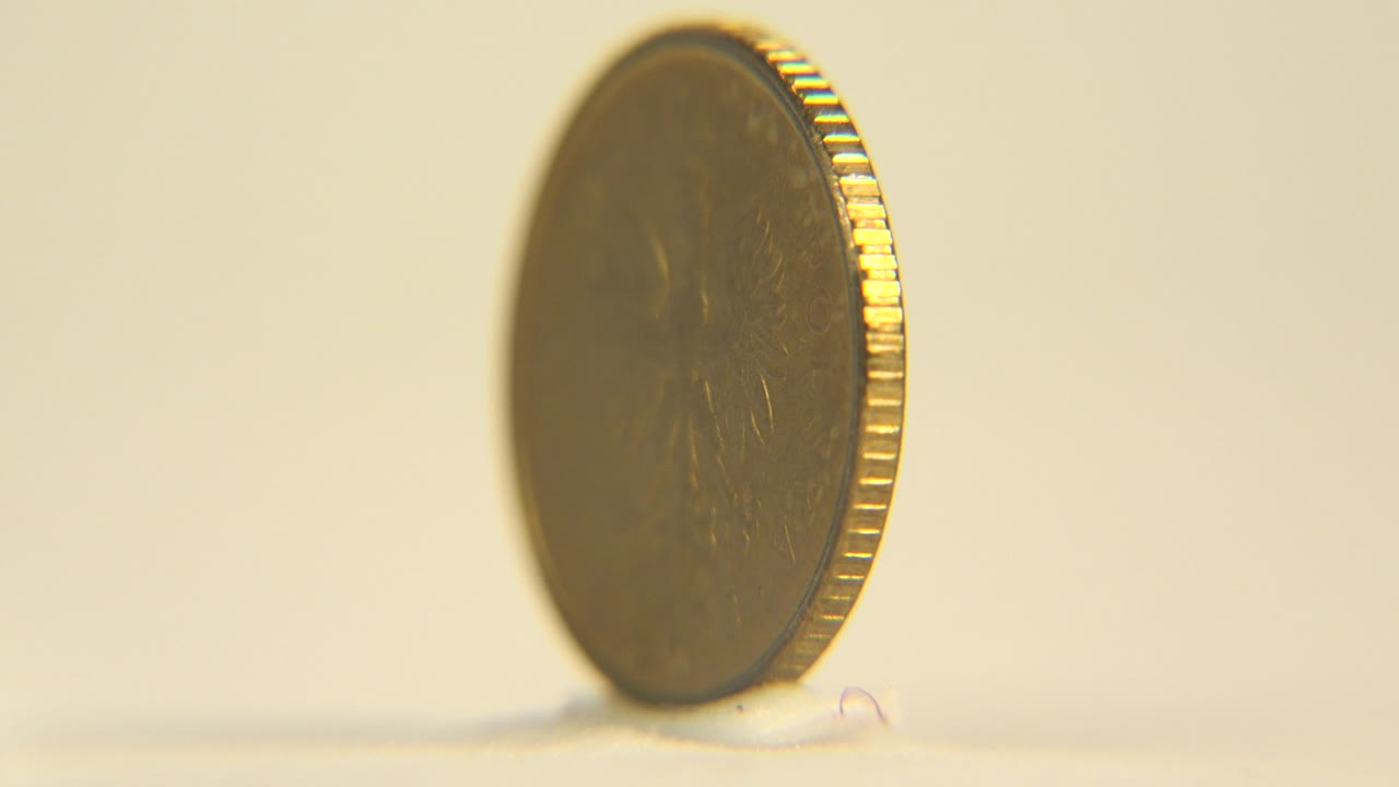 The coin has rotated into a partial face view on the right side of the frame, showing a dark gold face, bright rim highlights, pale surface, and no visible people.