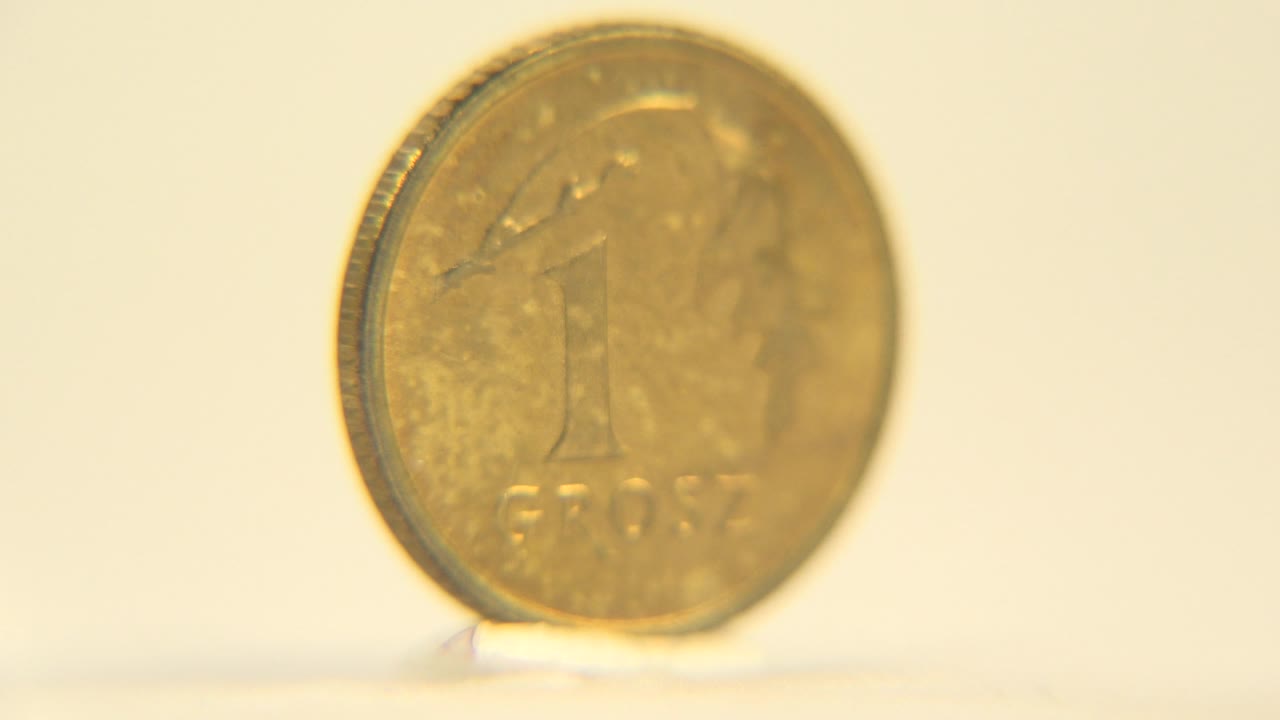A front view of the gold-colored coin shows a large number one and faint lower lettering, set against a warm plain background with no visible people.