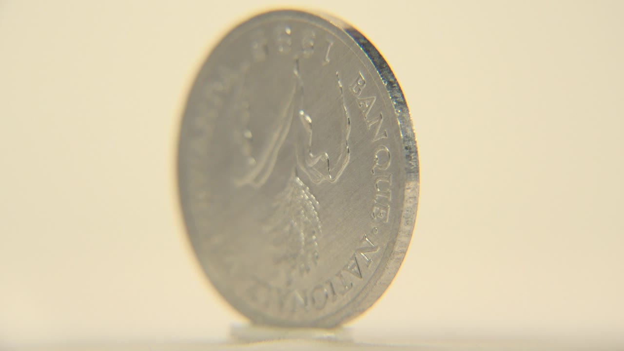A silver UN Franc coin stands angled on a pale tabletop with warm cream background light and no visible people.
