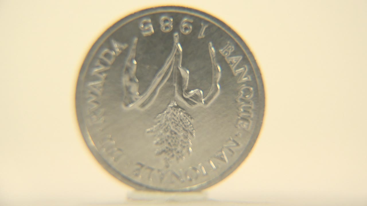 The coin faces the camera more directly, showing 1998 text around the rim and a raised central emblem against the warm plain background, with no visible people.