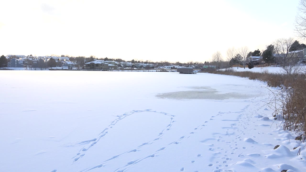 Snow covered frozen lake with footprints and distant homes