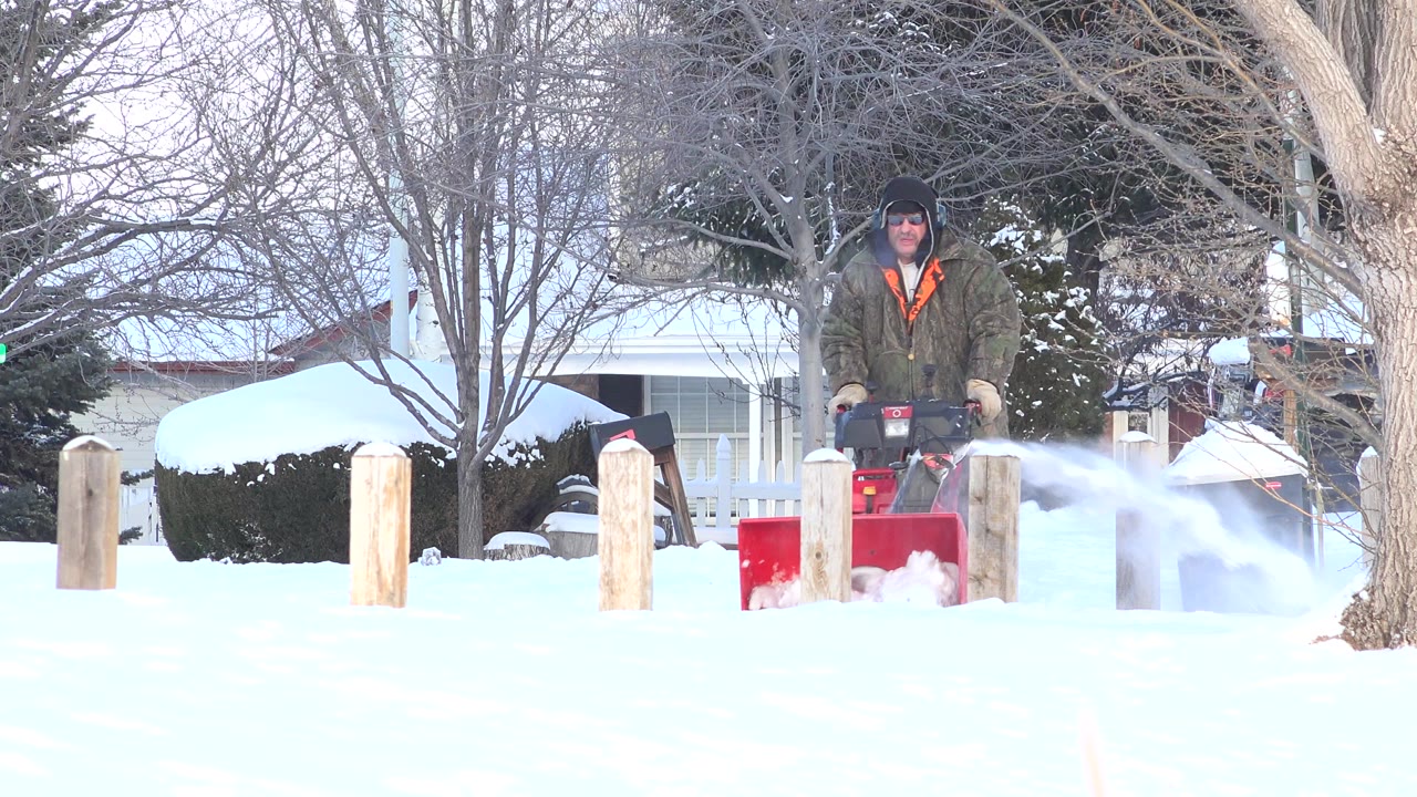 Man using a red snow blower in a snowy residential yard.