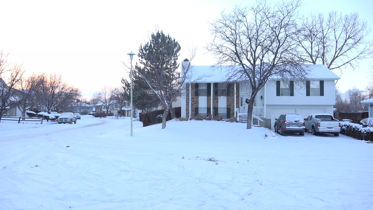 A snow-covered residential street in Hidden Lake, Colorado shows two-story homes, parked cars, bare trees, a lamppost, and no visible people at the start of the clip.