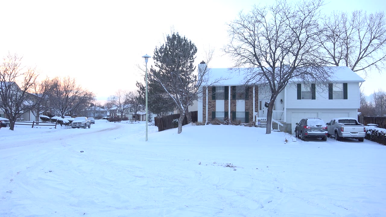 Two-story house and parked cars beside a snow-covered road.