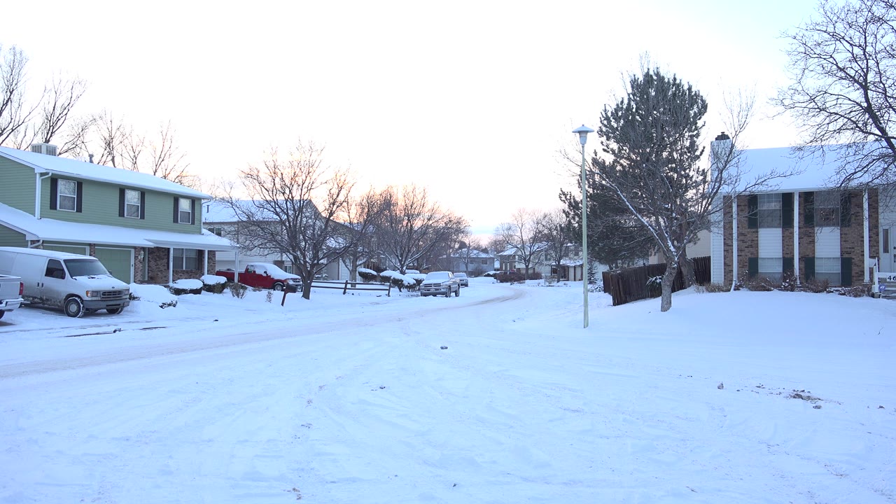 Early pan position showing green-sided homes, a white van, a red car, snow-covered roofs, bare trees, and no visible people in Hidden Lake, Colorado.