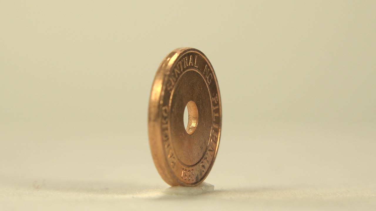 The coin rotates into a three-quarter view, revealing the drilled center hole and raised circular lettering on its warm metal face, with no visible people.