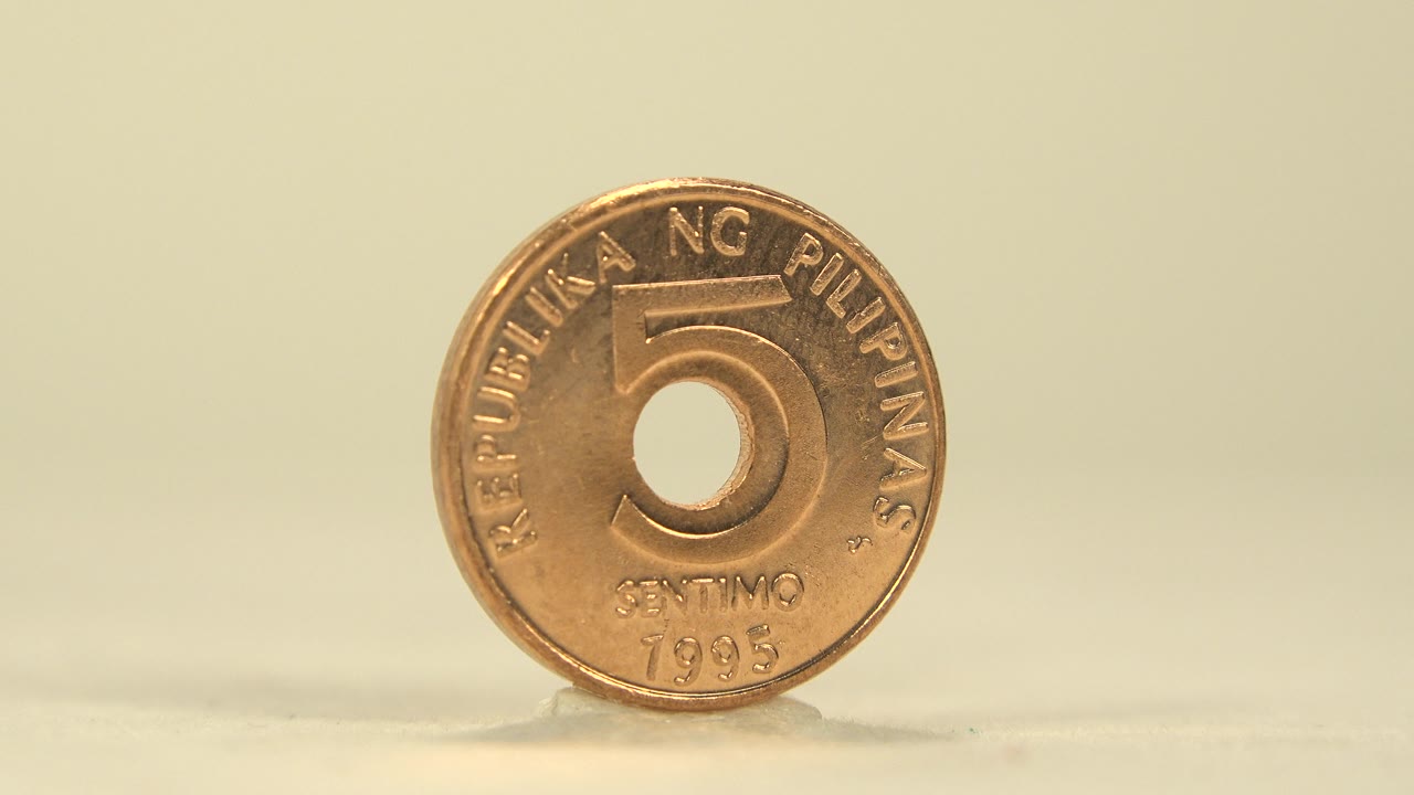 Front face of a copper-colored Philippine 5 sentimo coin stands upright on a pale surface against a warm cream background, with no visible people.