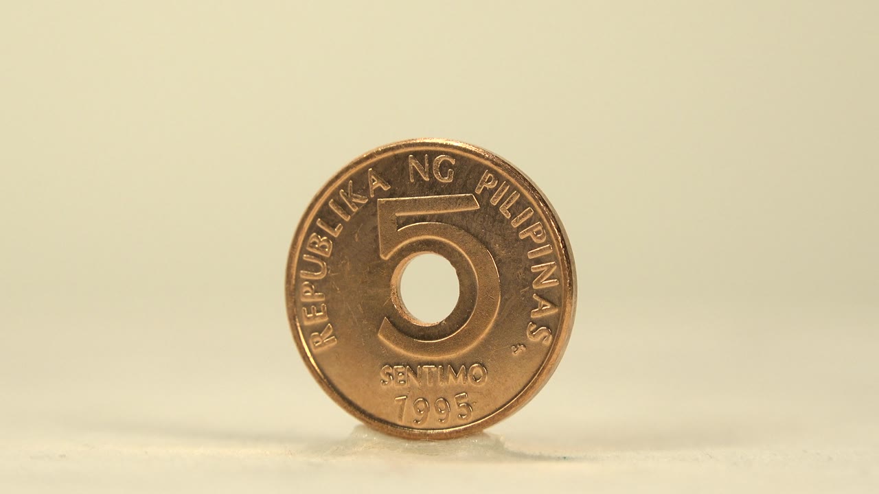 Front-facing Philippine five centavo coin near the right side of the frame, standing on the same pale surface with a soft shadow and no visible people.