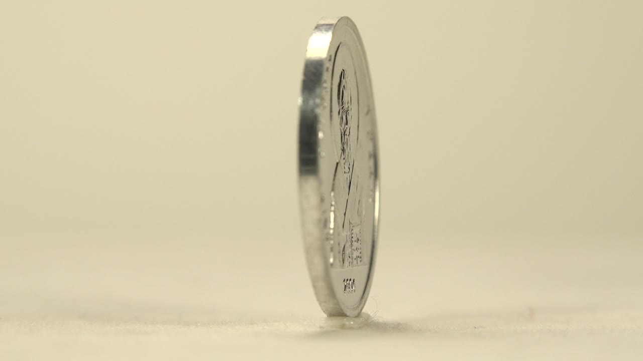 A silver coin stands nearly edge-on at the left side of a pale tabletop frame, with soft beige background and no visible people.