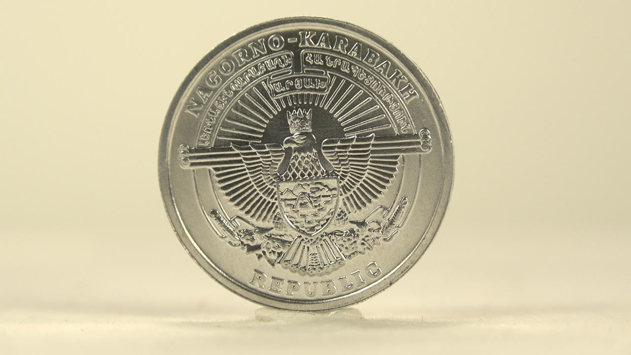 A similar frontal view keeps the emblem side centered, with the coin upright on the pale surface and soft highlights along its rim, with no visible people.