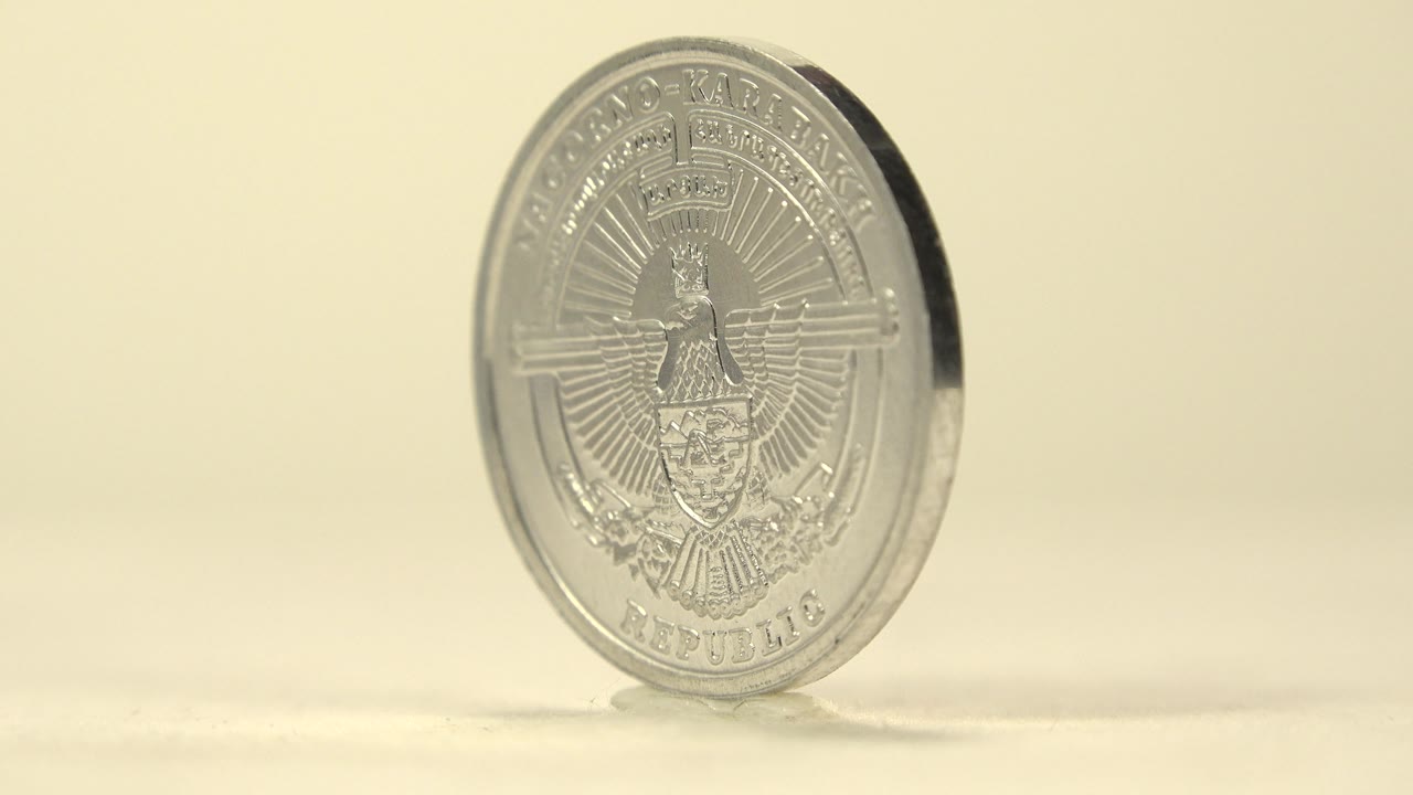The coin is turned to a three-quarter angle, showing its narrow dark edge and faint front-side engravings against the warm neutral background, with no visible people.