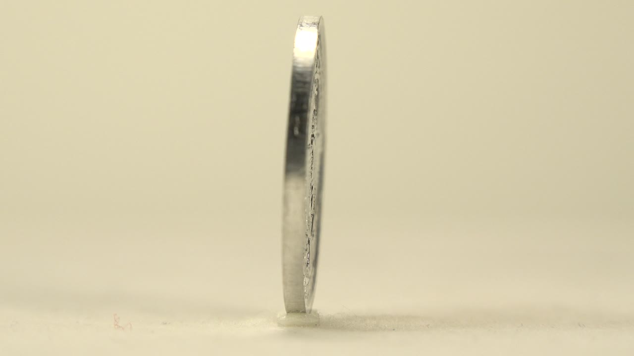 Silver coin seen mostly edge-on while rotating upright.