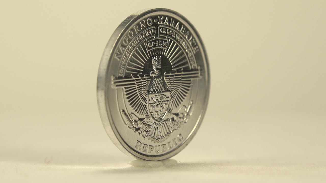 An engraved face of the silver coin turns toward the camera, showing a detailed emblem and lettering on the reflective metal with no live people visible.