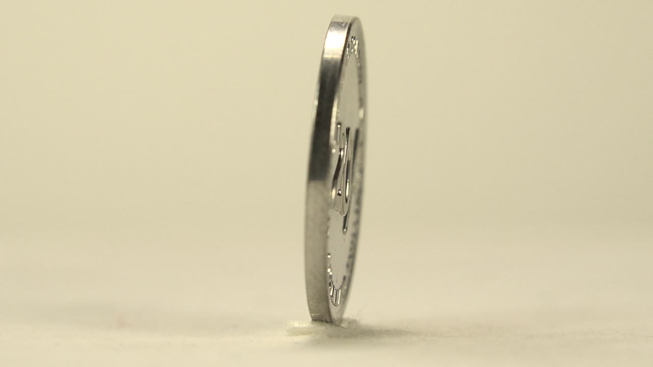 A narrow side view shows the coin almost edge-on, standing on the pale tabletop with only a sliver of its face visible and no visible people.