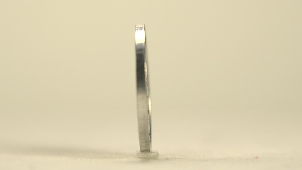 Upright Croatian silver coin seen edge-on near the center of a pale frame, with a small base shadow and no visible people.