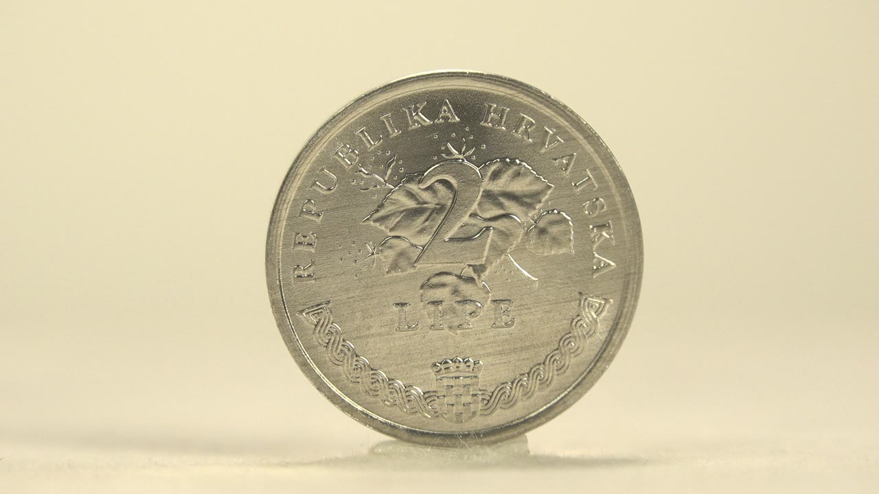 A silver-colored Croatian 25 lipa coin stands upright on a pale tabletop against a warm cream background, with no visible people.