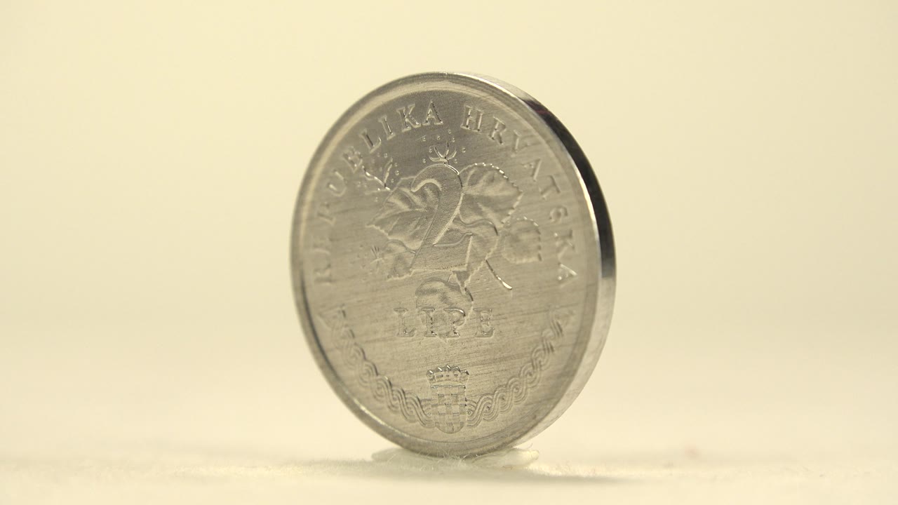 The coin has rotated to a slight angle, showing the dark rim along one edge while the 25 lipa face remains partly visible and no people appear.