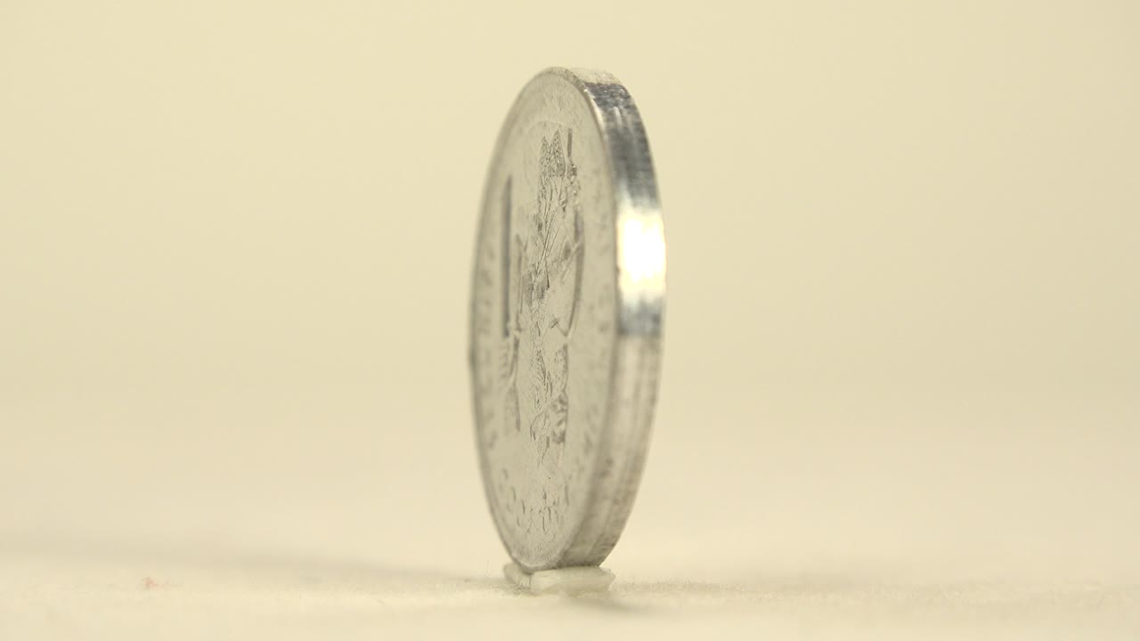 A silver coin stands on its edge on a pale tabletop in Italy metadata, seen from a narrow side angle with no visible people.