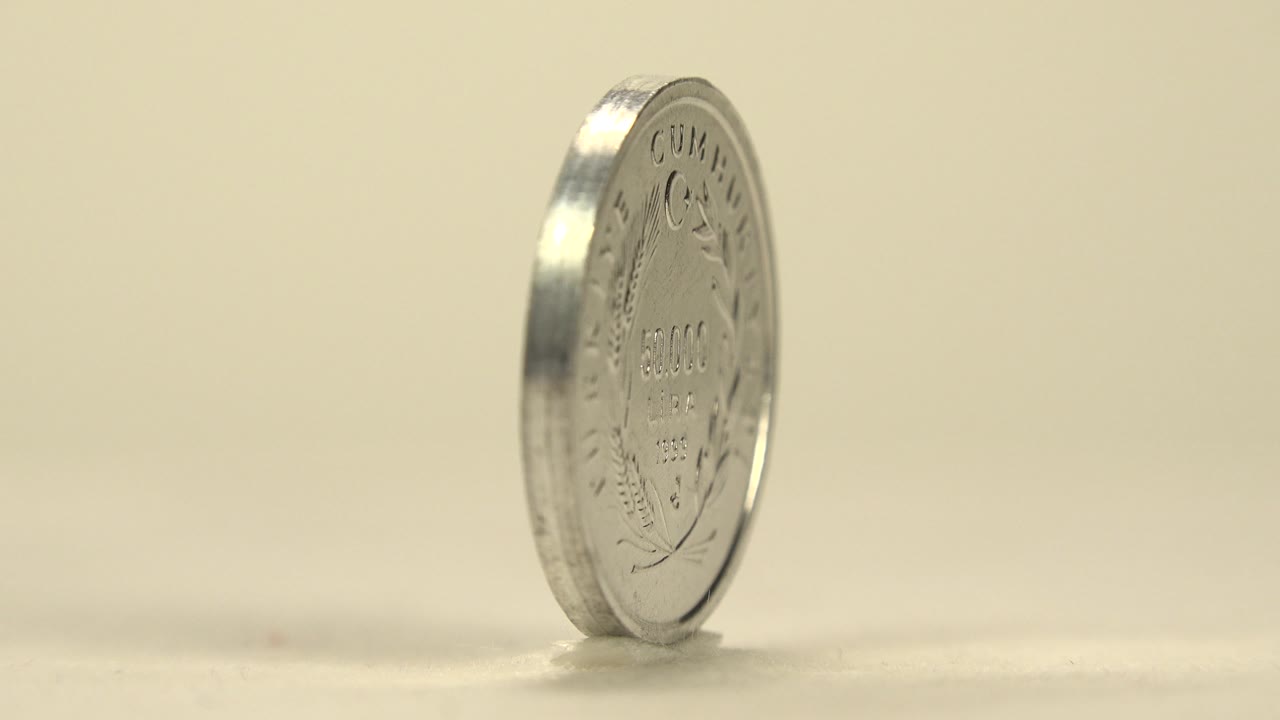 A silver coin marked with Lira text turns at a slight angle on the pale tabletop, showing part of the engraved face and no visible people.