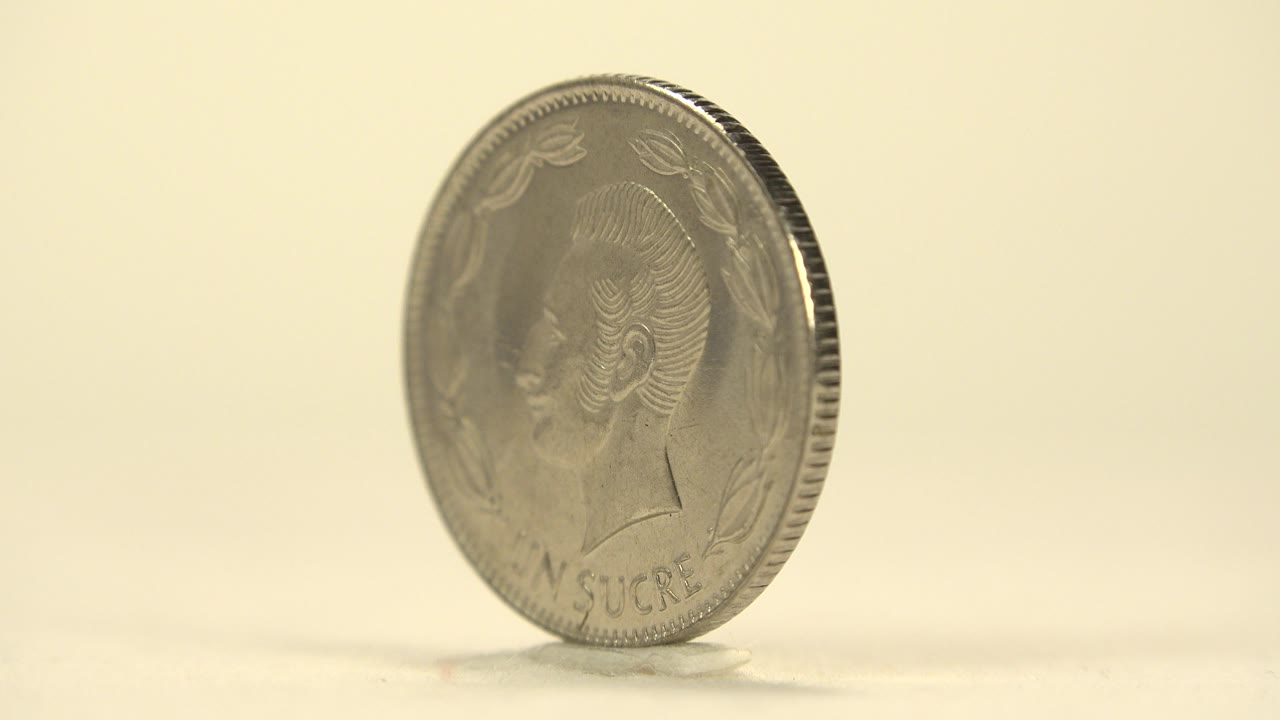 A small silver-toned coin leans upright on a cream surface with its portrait side partly visible and no visible people.