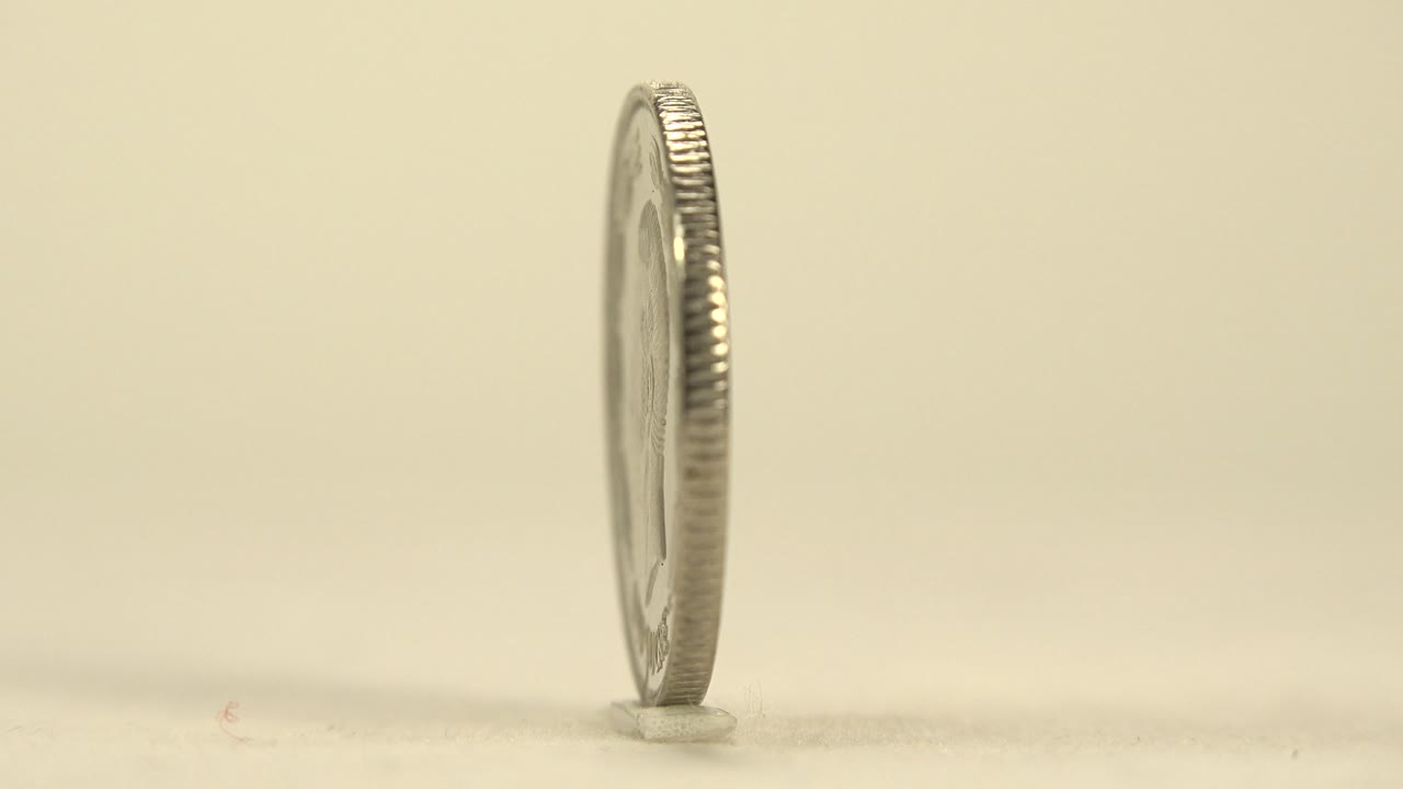 The coin turns nearly edge-on, showing a narrow ridged profile above the cream surface with no visible people.