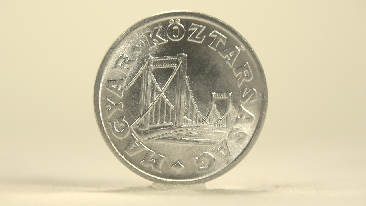 A silver coin stands upright on a pale surface with the engraved bridge side facing forward, warm light, and no visible people.