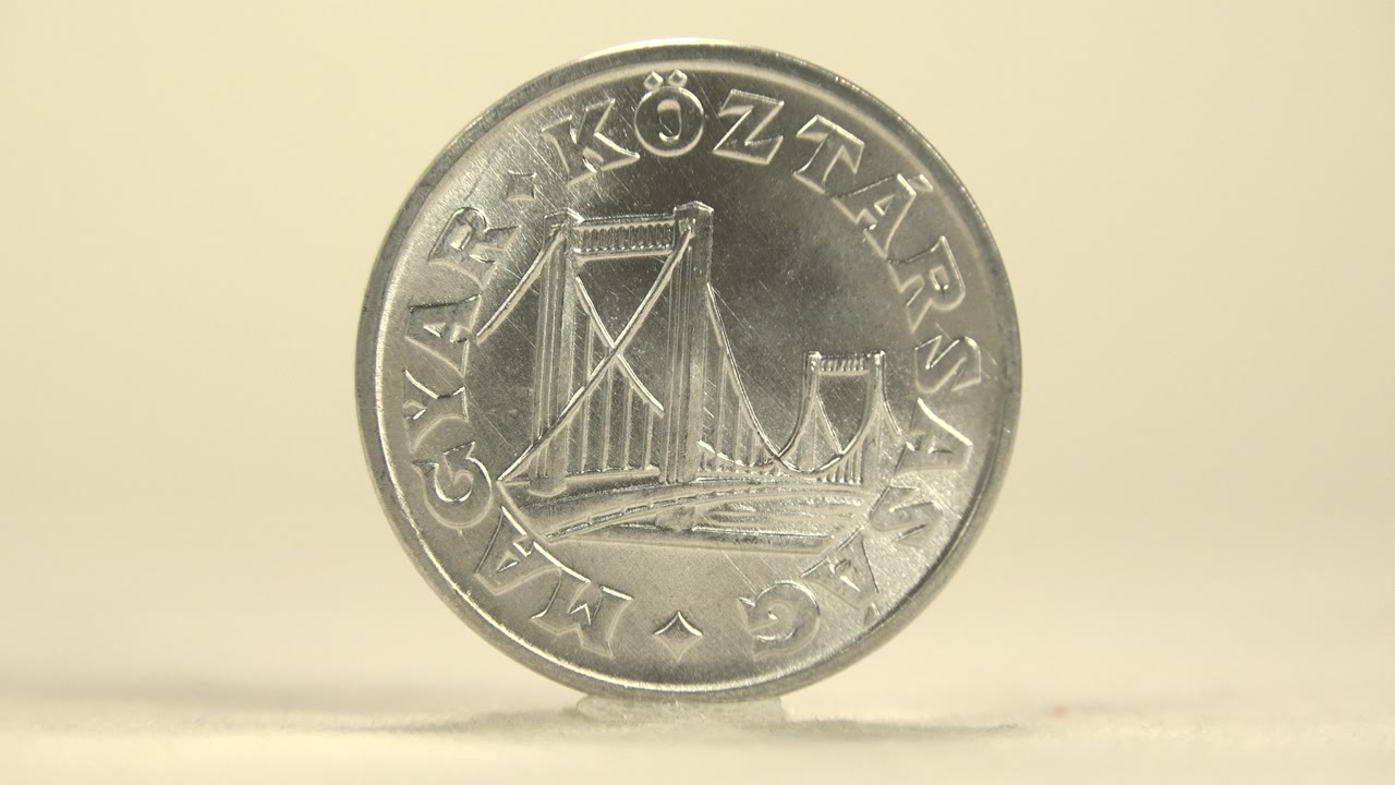 The upright silver coin remains nearly face-on, with bridge engraving and circular text centered against a cream background and no visible people.