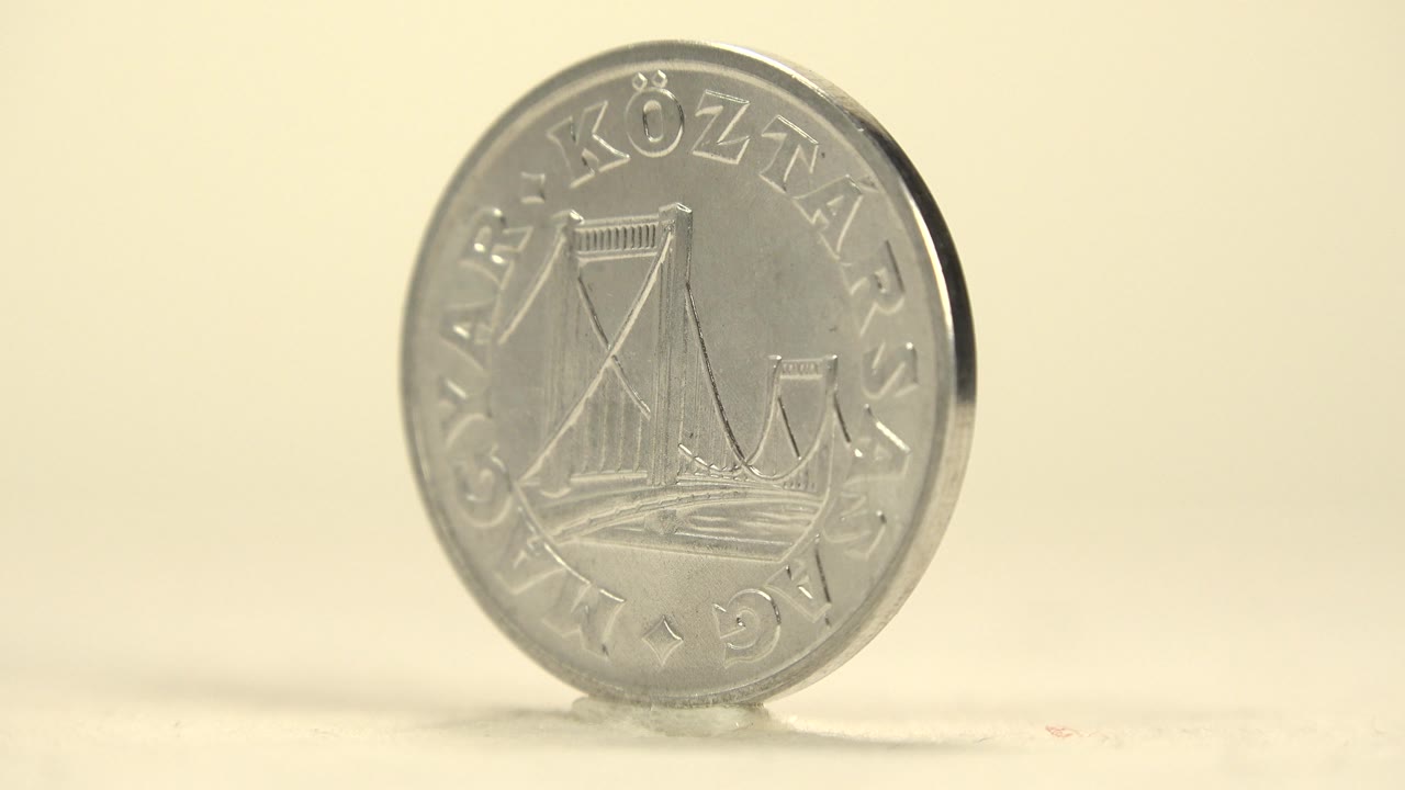 The coin has rotated to a slight angle, keeping the bridge side visible while showing a darker rim edge, with no visible people.