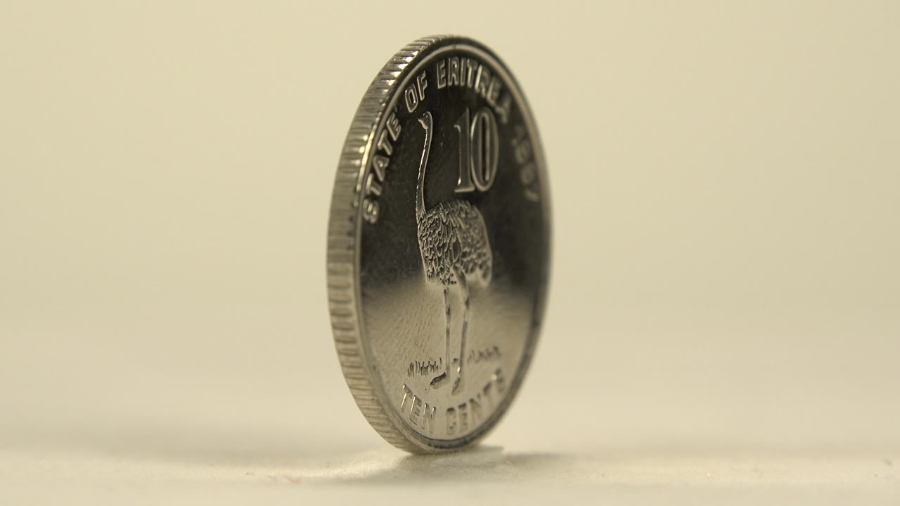 A silver ten cent coin turns toward camera, showing the number 10, an animal figure, rim lettering, and no visible people.
